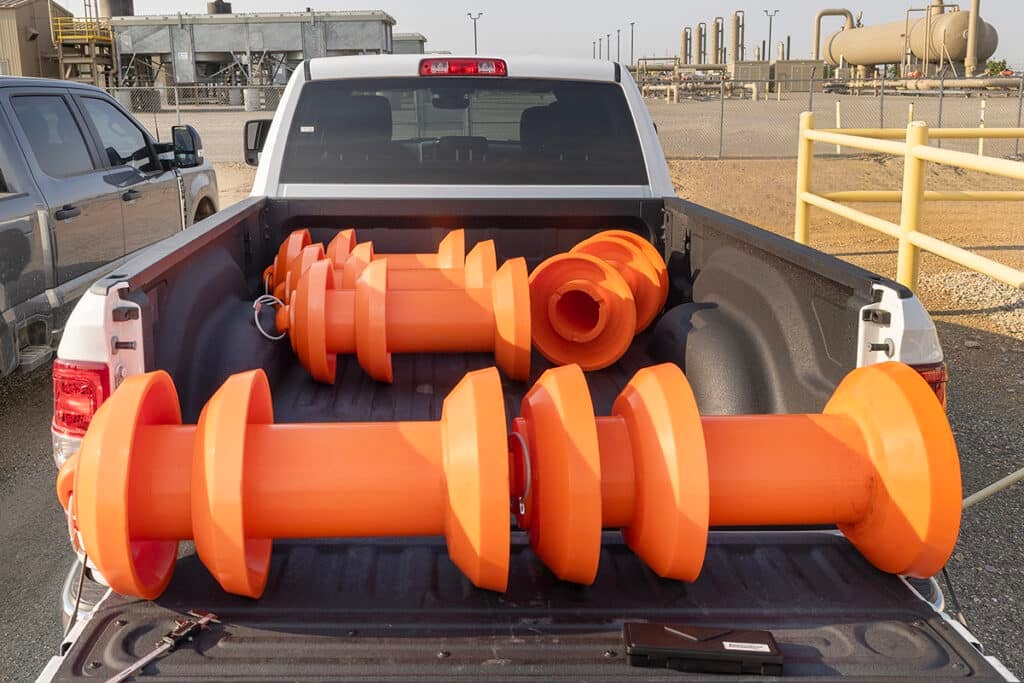 Five orange pipeline pigs in a truck bed at a job site. Two are sitting end to end on the tailgate to demonstrate how they would load into the pigging unit.